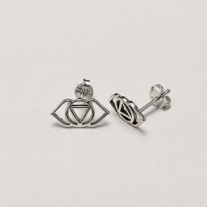 Op de afbeelding: Een paar zilveren oorknopjes met een gestileerde oogvorm en een centraal ontwerp van een driehoek en cirkel. Elke oorbel heeft een stift en is gestempeld met 925 voor sterling zilver, met een gepolijste metalen afwerking.