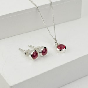 Può includere: Un set di orecchini e una collana d'argento con accenti di pietre preziose rosse.