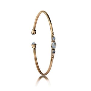 May include: A gold bangle bracelet with a row of moonstone gemstones. The bracelet is open and has a simple design.