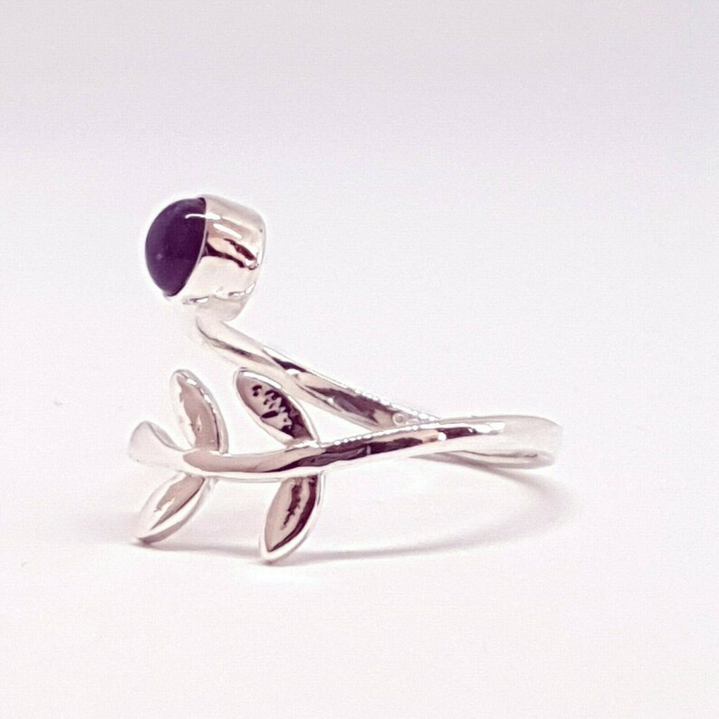 May include: A silver ring with a dark purple stone and a delicate branch design with leaves.