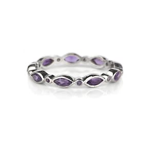 May include: A silver ring featuring a repeating pattern of marquise-cut purple gemstones. The ring's design includes alternating larger marquise stones and smaller round stones, creating a continuous, elegant band. The ring is set against a white background.