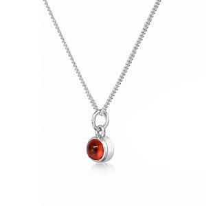 May include: A silver-toned metal chain necklace featuring a small, circular pendant with a polished silver setting and a smooth, translucent red gemstone at its center. The pendant hangs from a simple silver jump ring attached to the chain.