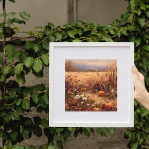 May include: A framed landscape painting depicting a field of wildflowers and pumpkins in autumn colors. The artwork features a warm palette of oranges, yellows, and purples, with a white frame. The painting evokes a sense of harvest and seasonal beauty.
