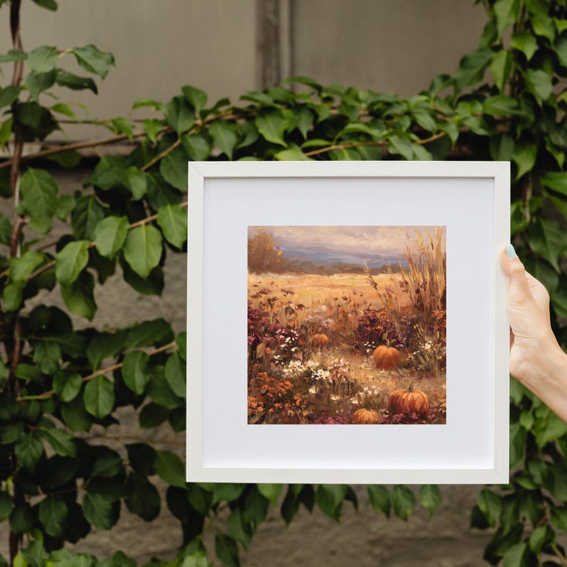 May include: A framed landscape painting depicting a field of wildflowers and pumpkins in autumn colors. The artwork features a warm palette of oranges, yellows, and purples, with a white frame. The painting evokes a sense of harvest and seasonal beauty.