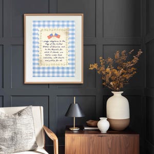May include: Framed print featuring the Pledge of Allegiance against a blue and white gingham background. The print includes two American flags and star accents, encased in a light wood frame. The artwork is displayed on a dark gray paneled wall.