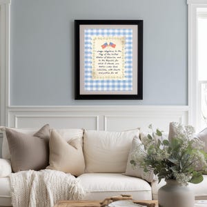 May include: A framed print featuring the Pledge of Allegiance. The text is set against a blue and white gingham pattern, with a border of stars and two small American flags. The frame is black.