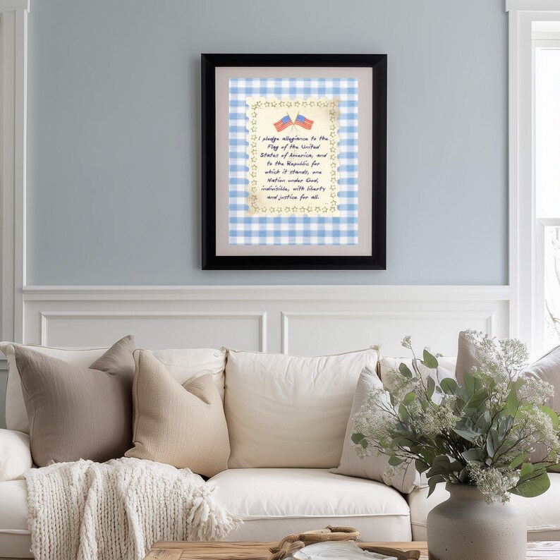 May include: A framed print featuring the Pledge of Allegiance. The text is set against a blue and white gingham pattern, with a border of stars and two small American flags. The frame is black.
