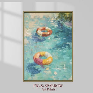 May include: An art print of a pool scene with two colorful inflatable rings floating on the water. The water is painted in shades of blue and turquoise, with the rings in orange, yellow, and pink. The print is framed in a gold-colored frame. The text "FIG & SPARROW Art Prints" is at the bottom.