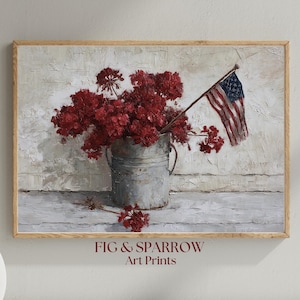 Puede incluir: Una impresión artística enmarcada que presenta una composición de naturaleza muerta. Un cubo de metal galvanizado contiene flores rojas vibrantes y una pequeña bandera estadounidense. El fondo tiene una apariencia texturizada blanquecina, con el texto "FIG & SPARROW Art Prints" en la parte inferior.
