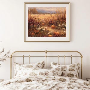 May include: A framed landscape painting depicts a field of pumpkins, flowers, and tall grass in autumn colors. The painting hangs above a bed with a gold metal frame and floral patterned bedding.