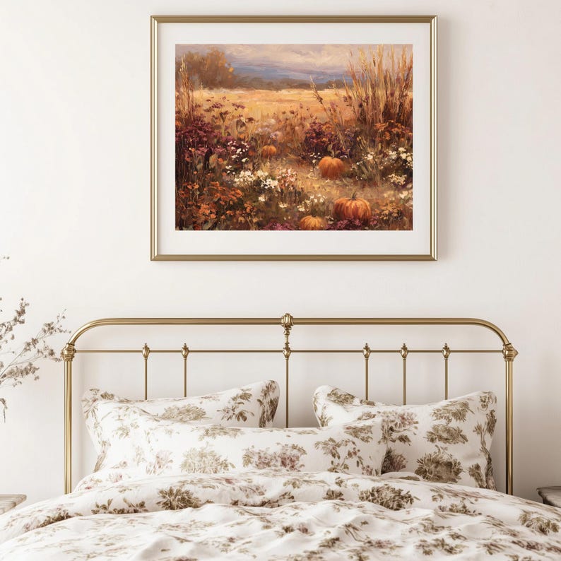 May include: A framed landscape painting depicts a field of pumpkins, flowers, and tall grass in autumn colors. The painting hangs above a bed with a gold metal frame and floral patterned bedding.