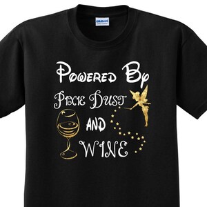 May include: Black t-shirt with gold glitter text that reads "Powered by Pixie Dust and Wine". A gold glitter fairy with wings is flying above the text. A glass of wine is to the left of the text.