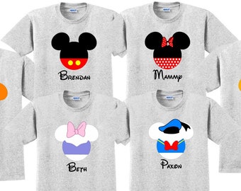 May include: Six grey t-shirts with different Disney character heads printed on them. The characters are Mickey Mouse, Minnie Mouse, Goofy, Donald Duck, and Pluto. Each shirt has a name printed below the character head. The names are Brendan, Mummy, Greg, Beth, Paxon, and Olivia.