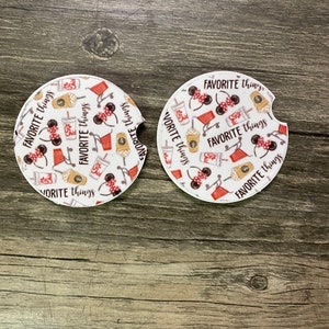 May include: Two white round car coasters with a black and red Mickey Mouse design. The coasters feature a pattern of Mickey Mouse ears, coffee cups, shopping carts, and the text "FAVORITE things".
