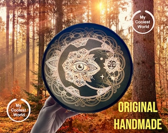 May include: A round, dark blue decorative tray with a celestial design featuring a crescent moon, sun, and an eye symbol in silver. The tray has the words "ORIGINAL HANDMADE" in white. The tray is being held in front of a forest background.