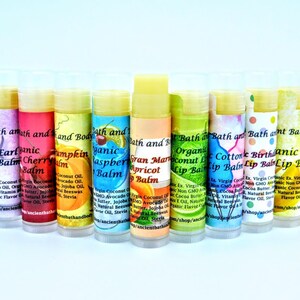 May include: A row of 12 colorful lip balms in tubes with various fruit and floral scents. The lip balms are labeled with the brand name "Bath and Body" and the scent name. The lip balms are arranged in a rainbow pattern.