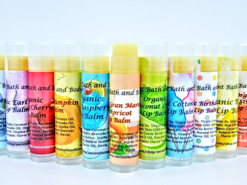 May include: A row of 10 colorful lip balms with various flavors, including cherry, pumpkin, raspberry, apricot, coconut lime, cotton candy, birthday cake, and strawberry. Each balm is labeled with the name of the flavor and the words "Bath and Body" and "Organic Lip Balm".