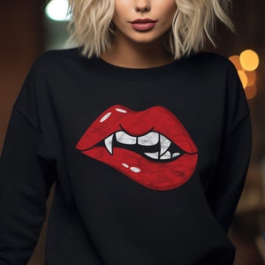 May include: A woman with blonde hair is wearing a black sweatshirt with a red, cartoon-style mouth with fangs on it.