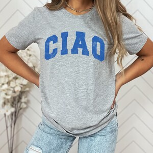 May include: A gray t-shirt with a blue "CIAO" graphic printed on the front. The shirt is made of a soft, comfortable material and has a relaxed fit.