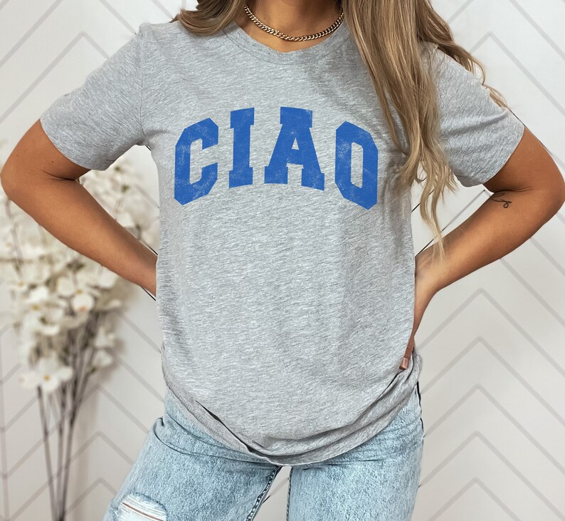 May include: A gray t-shirt with a blue "CIAO" graphic printed on the front. The shirt is made of a soft, comfortable material and has a relaxed fit.