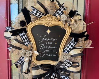 May include: A Christmas wreath with a gold-framed chalkboard that reads "Jesus is the Reason for the Season." The wreath features burlap, black and white checkered ribbons, and black velvet ribbons. The wreath is hanging on a red door.