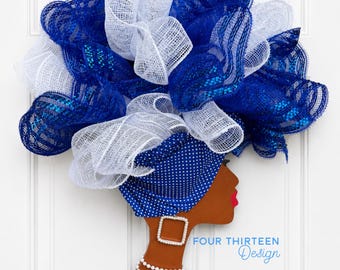 May include: A decorative wall hanging featuring a profile silhouette of a person with brown skin, red lips, and a blue polka-dot headwrap. The hair is made of blue and white mesh ruffles. It includes a square earring, a pearl necklace, and the text FOUR THIRTEEN Design.