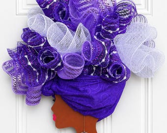 May include: A wall decoration featuring a profile silhouette of a person with dark skin, wearing a purple patterned headwrap, a gold hoop earring with a purple flower, and a white beaded necklace. The hair is made of purple and white mesh loops.