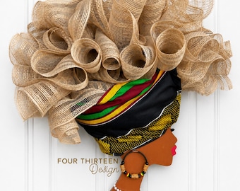 May include: A wall hanging featuring a profile silhouette of a person with brown skin, wearing a headwrap with black, yellow, green, and red stripes. The headwrap is adorned with voluminous tan mesh ruffles. Includes a hoop earring and white necklace.