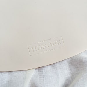 May include: A close-up of a white, round, silicone mat with the text "made of HONOUR company" embossed in the lower right corner.
