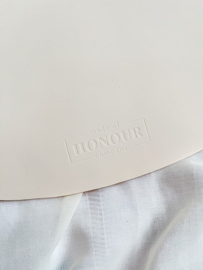 May include: A close-up of a white, round, silicone mat with the text "made of HONOUR company" embossed in the lower right corner.
