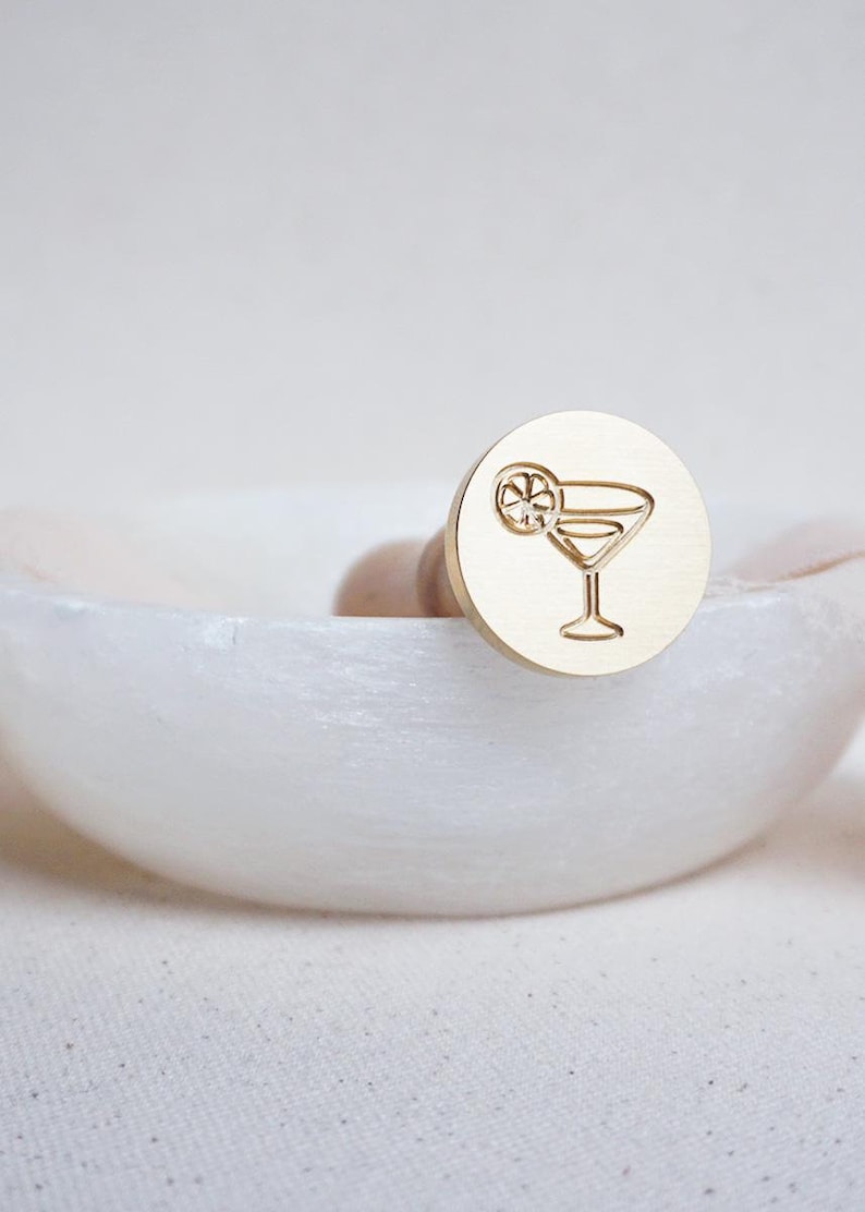 May include: A gold-toned metal wax seal stamp with a design of a martini glass with a lime wedge.