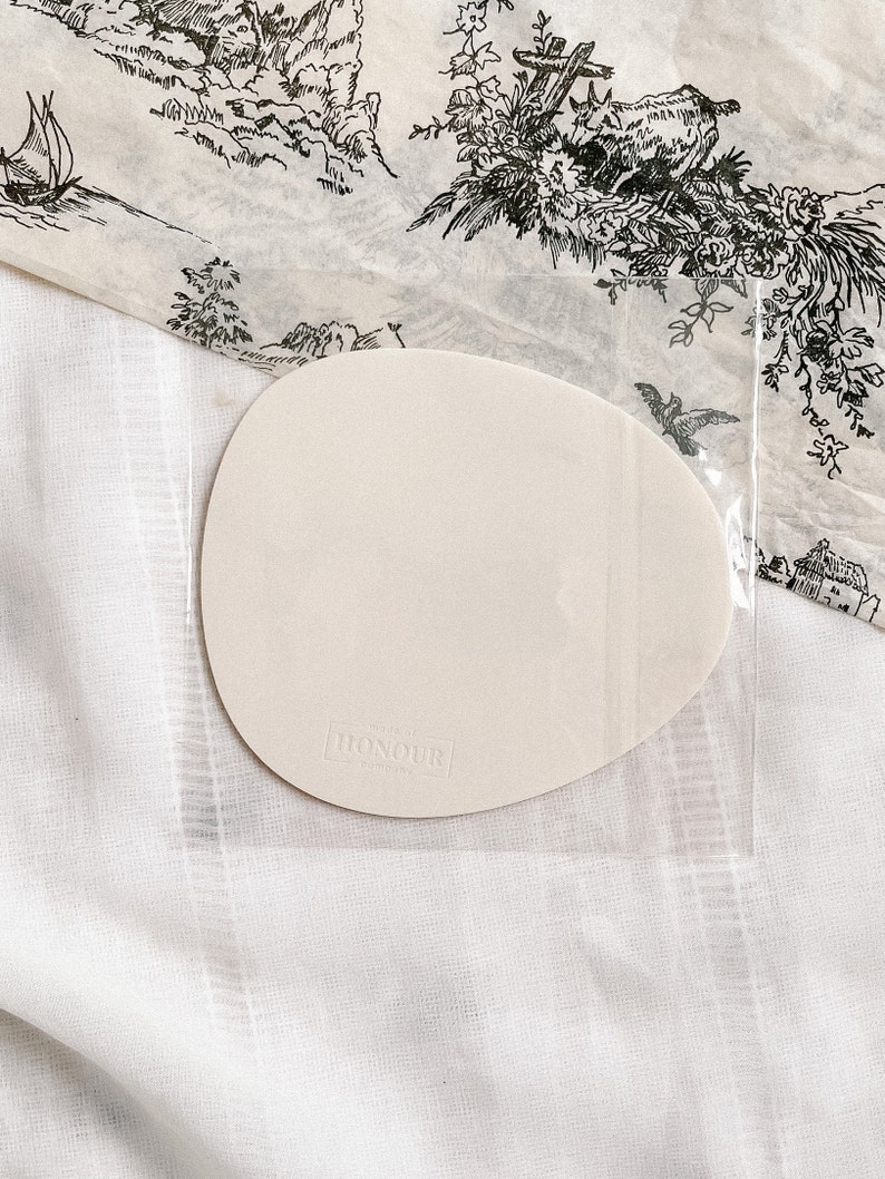 May include: A white, oval-shaped, blank card with the text "HONOUR LONDON" printed in black on the bottom. The card is sitting on a white, textured surface.
