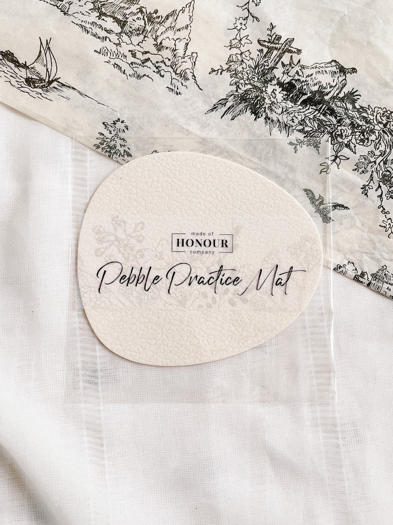 May include: A round, off-white, textured pebble practice mat with the text "Pebble Practice Mat" and "made of HONOUR company" printed in black.