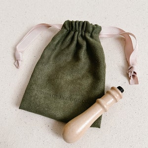 May include: A wooden stamp handle with a black top, in a green velvet drawstring bag with a pink ribbon. The bag has the text "A Love Of Honour" printed on it.