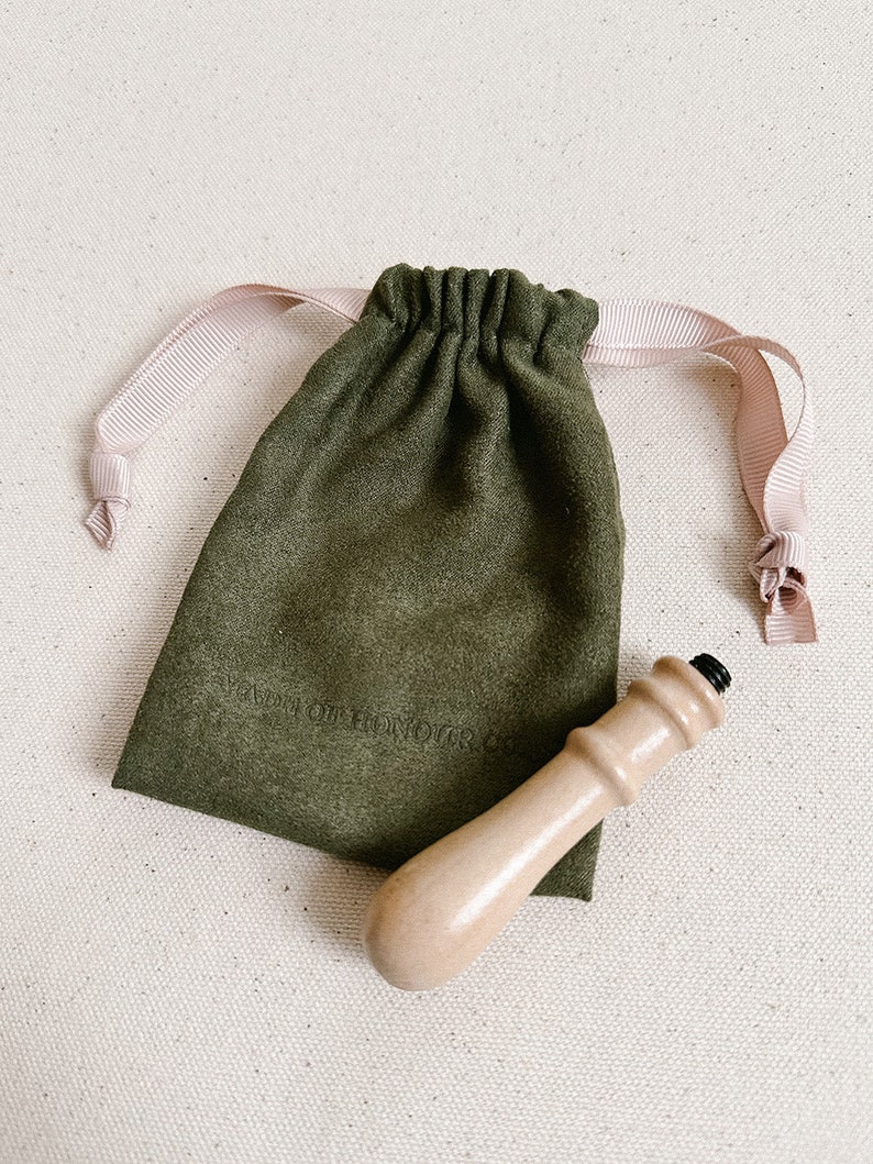 May include: A wooden stamp handle with a black top, in a green velvet drawstring bag with a pink ribbon. The bag has the text "A Love Of Honour" printed on it.