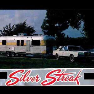 May include: A white car with a silver and yellow travel trailer behind it. The trailer has the words "Silver Streak" on the side.