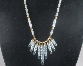 May include: A clear glass and gold beaded necklace with a teardrop-shaped pendant. The necklace is displayed on a black velvet bust form.