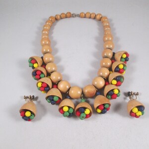 Può includere: Un set di collana e orecchini in legno con grandi perline di legno marrone e perline più piccole colorate. La collana ha una chiusura a clip e gli orecchini sono a clip.