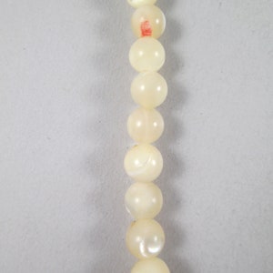 May include: A strand of white pearl-like beads with a slight iridescent sheen.