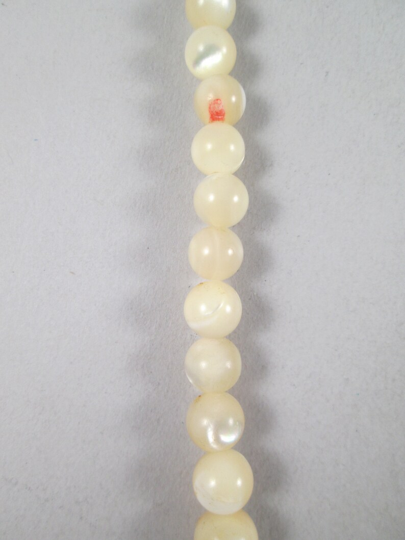 May include: A strand of white pearl-like beads with a slight iridescent sheen.