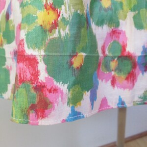 Op de afbeelding: Een witte stoffen rok met een kleurrijke abstracte bloemenprint in tinten roze, groen, geel en blauw. De rok heeft een witte zoom met een gestikte naad.