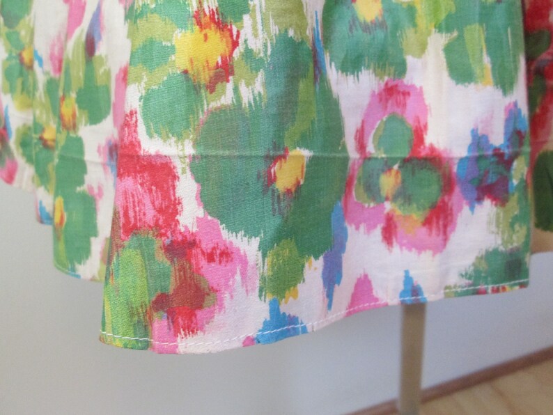 Op de afbeelding: Een witte stoffen rok met een kleurrijke abstracte bloemenprint in tinten roze, groen, geel en blauw. De rok heeft een witte zoom met een gestikte naad.