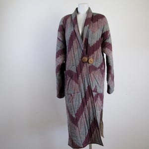 May include: A long, gray and purple quilted coat with a diagonal pattern and wooden buttons. The coat has a shawl collar and a long, flowing silhouette.