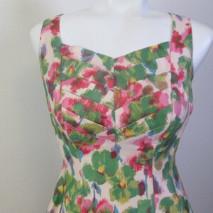 Op de afbeelding: Een mouwloze jurk met een bloemenprint in tinten roze, groen en wit. De jurk heeft een vierkante halslijn en een getailleerd bovenlijf.