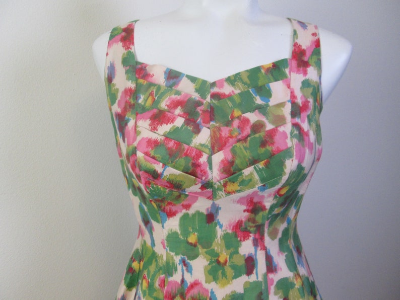 Op de afbeelding: Een mouwloze jurk met een bloemenprint in tinten roze, groen en wit. De jurk heeft een vierkante halslijn en een getailleerd bovenlijf.