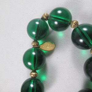 Pu&ograve; includere: Una collana di perline di vetro verde con accenti dorati. La collana ha un'etichetta che recita "KJL."
