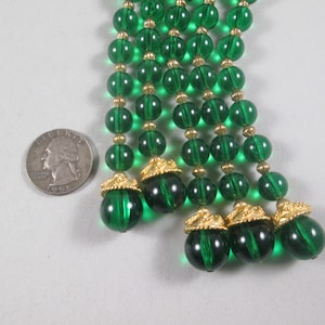 Pu&ograve; includere: Un lungo filo di perline di vetro verde smeraldo con accenti dorati. Le perline sono infilate su un filo dorato e hanno un aspetto a forma di nappa.