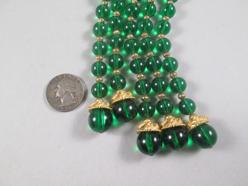 Pu&ograve; includere: Un lungo filo di perline di vetro verde smeraldo con accenti dorati. Le perline sono infilate su un filo dorato e hanno un aspetto a forma di nappa.