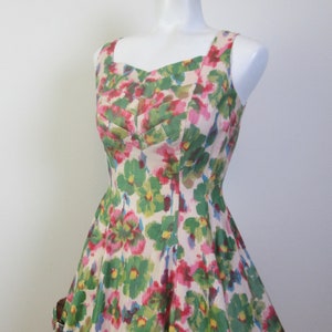 Op de afbeelding: Een mouwloze jurk met een bloemenprint in tinten roze, groen en geel. De jurk heeft een getailleerd bovenlijf en een volle rok.