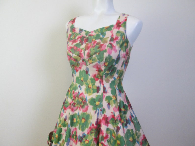 Op de afbeelding: Een mouwloze jurk met een bloemenprint in tinten roze, groen en geel. De jurk heeft een getailleerd bovenlijf en een volle rok.